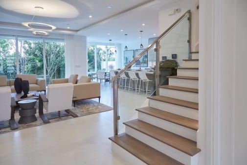 Stainless post glass railing rises along a white stair beside a bright modern living room.