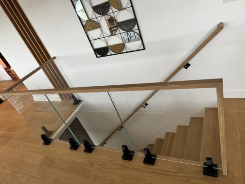 Overhead view of glass panels on black standoff pins with a white oak cap rail along an oak stair.