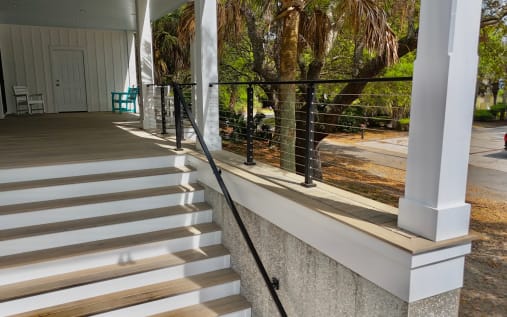Black cable railing between white porch columns with a matching black handrail down wide white steps.