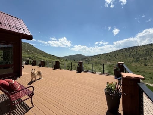 Wide composite deck edged by black cable railing and wood posts, looking out over a mountain valley.