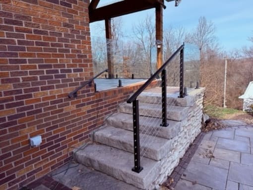 Black post cable railing alongside wide limestone steps beside a red brick wall.