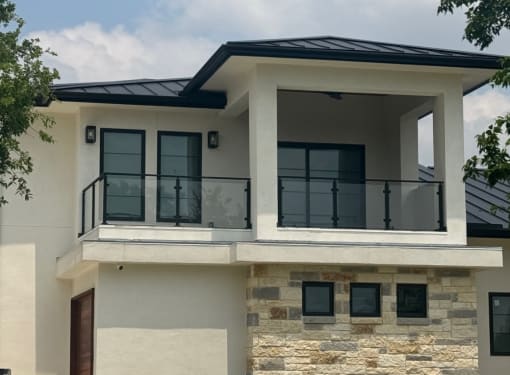 Modern stucco home exterior with two upper balconies enclosed by black-framed glass railings.