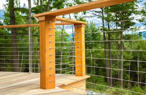 Cedar posts and cap rail with stainless cable infill around a wood deck in the forest.