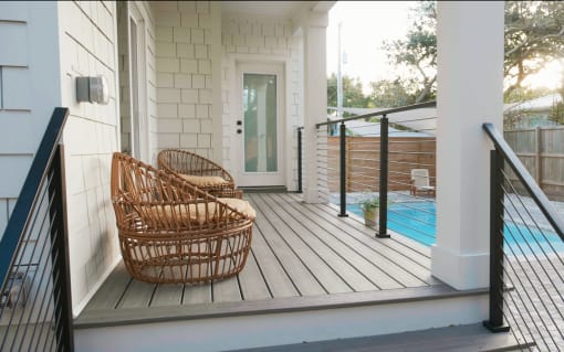 Black rod railing flanks steps from a white porch to a pool patio with wicker chairs.
