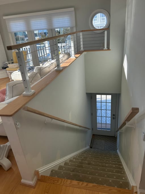 White posts and cable railing with wood cap rail guard a stair opening in a coastal-style home.
