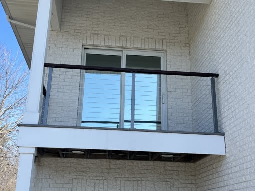Gray cable railing with a dark wood cap on a small balcony against white brick
