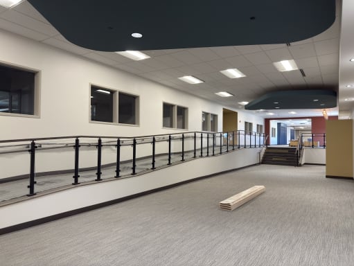Long accessible ramp lined with black-post glass railing and handrails in a commercial corridor