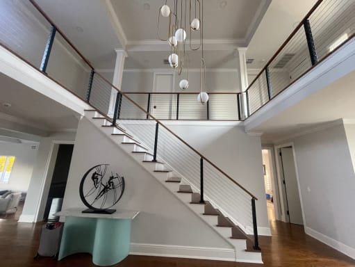 Black-post cable railing with walnut handrail runs up a white staircase and around an upper balcony in a two-story foyer.