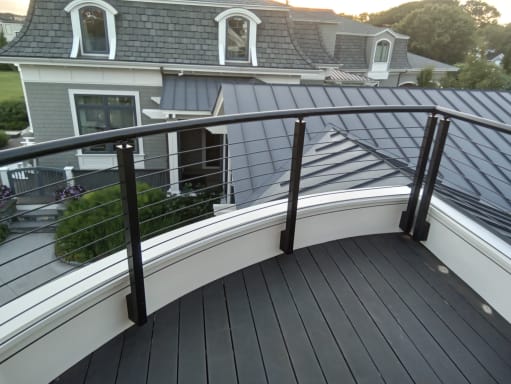 Curved black handrail and cable railing frame a dark-decked balcony above slate and metal rooftops.