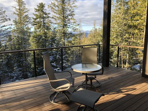 Black cable railing with wood cap around a covered deck looking out to snowy evergreens.