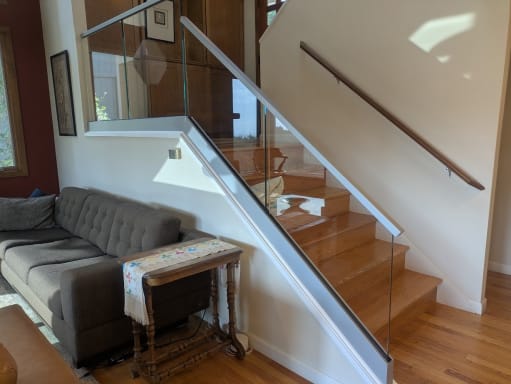Frameless glass in a base rail with stainless cap following a wood split-level stair beside a wall handrail.