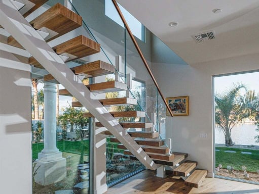 Thick wood treads on a white mono stringer with frameless glass on bright white ascend talons beside a window wall.
