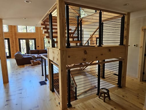 Black rod railing with square posts surrounds a timber switchback stair in a knotty-pine cabin great room.