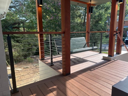 Black-post cable railing with wood top rail between cedar columns on a composite covered porch.