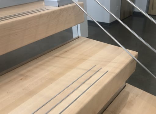 Close view of thick light maple treads with inset anti-slip grooves and slim metal rail infill.
