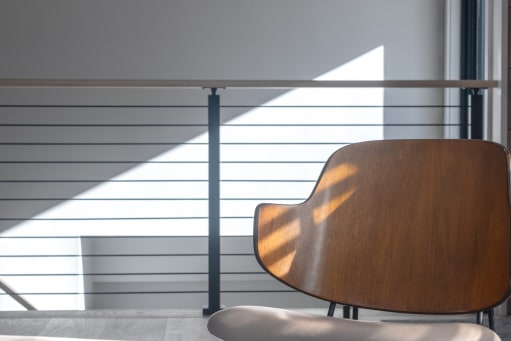 Black horizontal rod railing with wood cap in a sunlit room beside a molded wood chair.