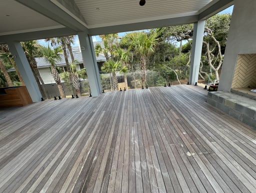 Frameless glass on black talon spigots edges a covered ipe deck with palm trees beyond