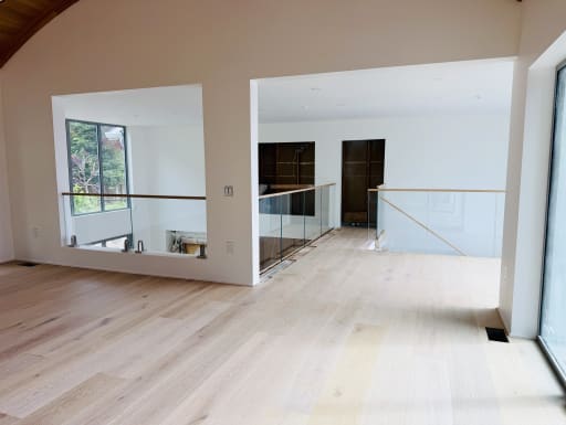 Glass railings with wood cap rails line interior openings across a wide oak-floored loft