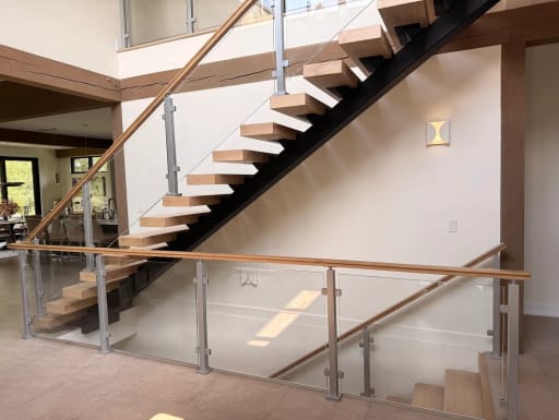Black mono stringer floating stair with silver posts, glass panels and wood handrail