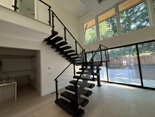 Dark wood floating stair on dual black stringers with post-to-post glass railing turning at a landing in a bright great room