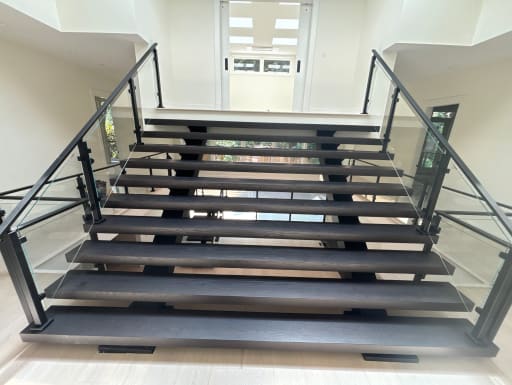 Extra-wide floating stair with dark treads on dual stringers flanked by black post glass railings