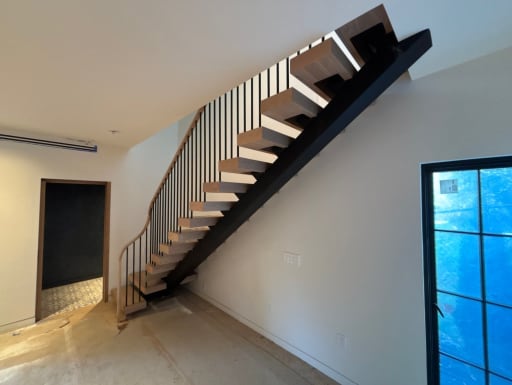 Black mono stringer floating stair with modern balusters and a curved oak handrail ending in a volute