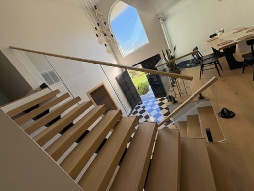 White oak floating stair with glass railing and wood handrail descending toward an arched entry