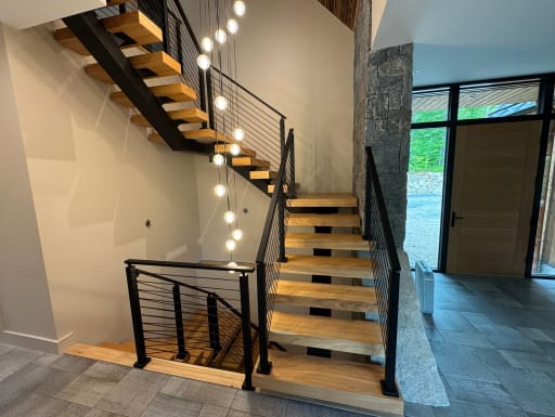 Oak floating switchback stair with black cable railing and a cascade of globe pendants beside a stone wall