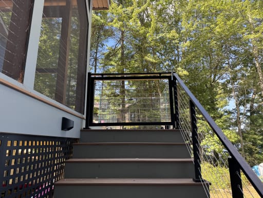 Black cable railing climbs exterior stairs to a jet black rod-infill gate
