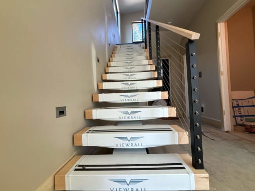 Floating stair in clean Viewrail tread covers with black cable railing and maple handrail