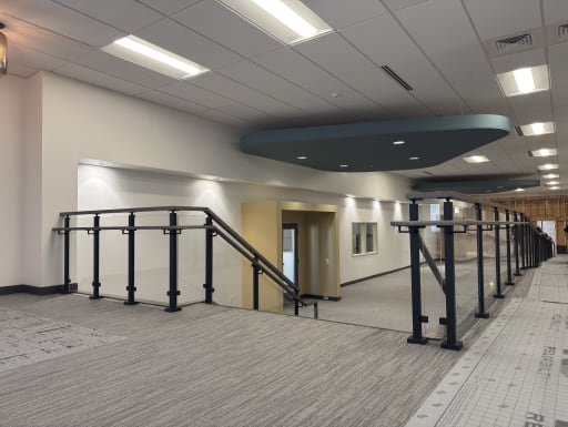 Black-post glass guardrail with handrails along a corridor stair and ramp
