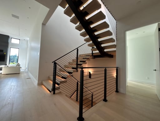 Floating stair with warm LED treads and black cable railing beside a living room
