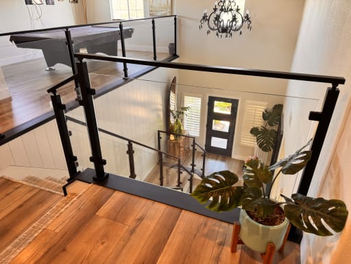 Black post glass railing lines a stair opening above a bright entry with a modern front door
