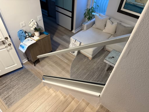 Frameless glass in a silver base rail with an aluminum cap guards a stair opening beside a living room