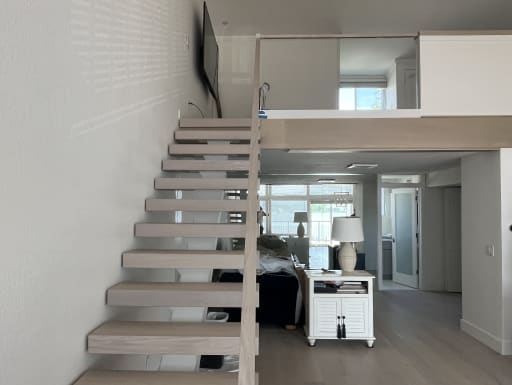 Whitewashed oak floating stair beside a frameless glass loft railing in a bright condo