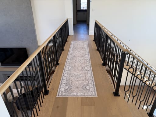 Black decorative iron baluster railing with oak handrails lines an upstairs bridge with a runner rug