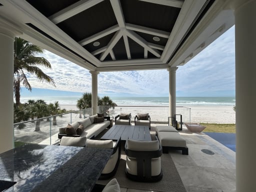 Frameless glass railing frames a covered beachfront lounge looking out to white sand and surf