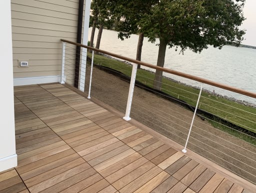 A hardwood deck corner with white cable railing posts and wood cap rail overlooking a lake.