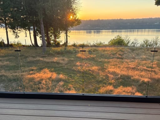 Frameless glass railing on a composite deck looks out over a meadow and lake at sunset.