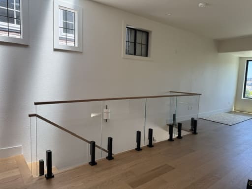 Frameless glass panels on black talon spigots with a wood cap rail guard a stair opening in a bright loft.