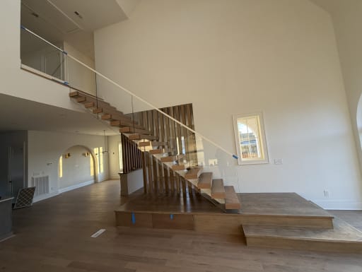 A FLIGHT Mono stair with oak treads and glass railing climbs from a wide stepped platform to a glass-railed loft.