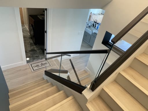 View down a light oak stair lined with glass panels set in a black channel with a black top rail.