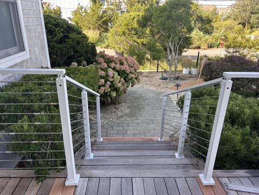 White-post cable railing frames hardwood deck steps leading down to a garden path with hydrangeas.