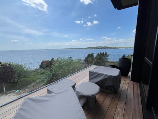 Frameless glass railing on a hardwood deck with covered lounge furniture and an open bay view.
