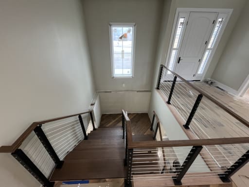 Black-post cable railing with a wood handrail surrounds an open wood stair and landing in a bright entry.