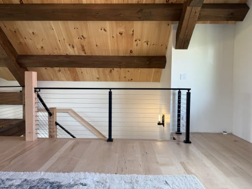 Black-post cable railing with wood newel guards a stair opening on a light hardwood loft.