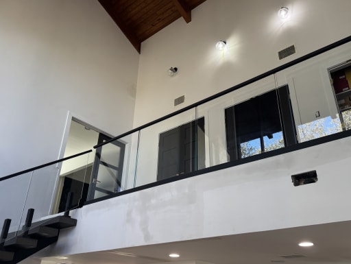 Frameless glass in a black base rail with black handrail lines a balcony above a dark FLIGHT stair.