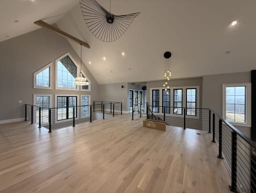 Black posts and handrail with horizontal cables enclose an open loft under a vaulted ceiling with tall gable windows.