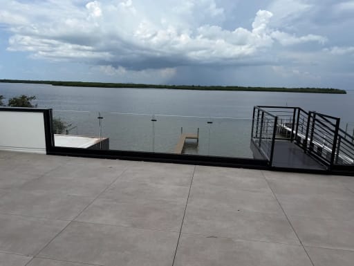 Frameless glass in a black base channel edges a tiled rooftop terrace overlooking a bay and boat dock.