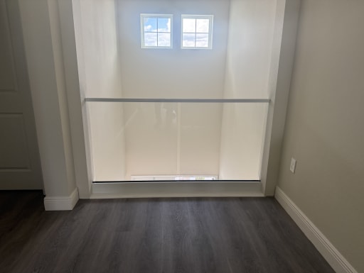 A single frameless glass panel in a white base shoe with top cap spans an open niche overlooking a two-story space.